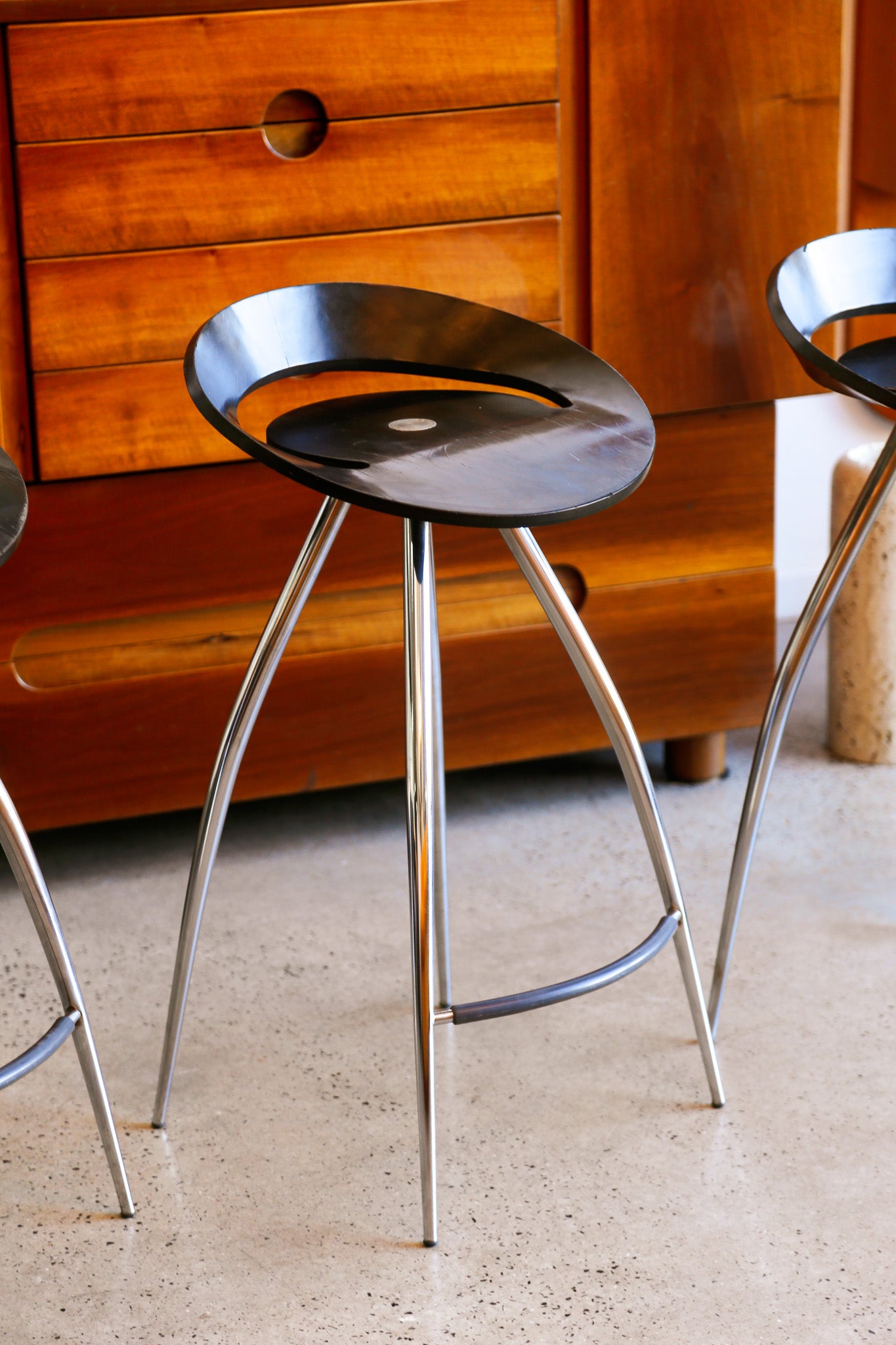 Modern bar stools with metal legs in front of a wooden cabinet.