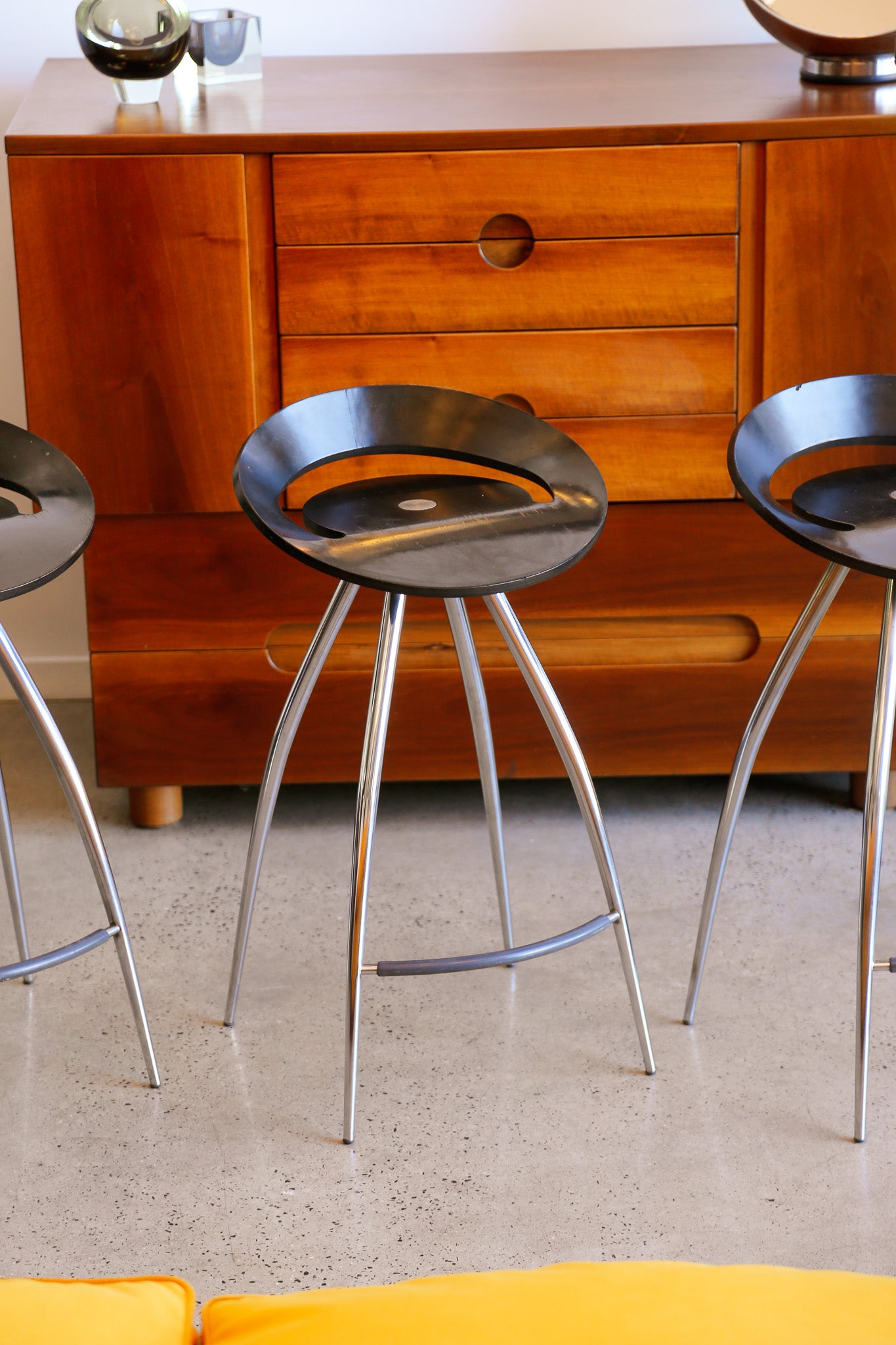 Three metal stools in front of a wooden cabinet.