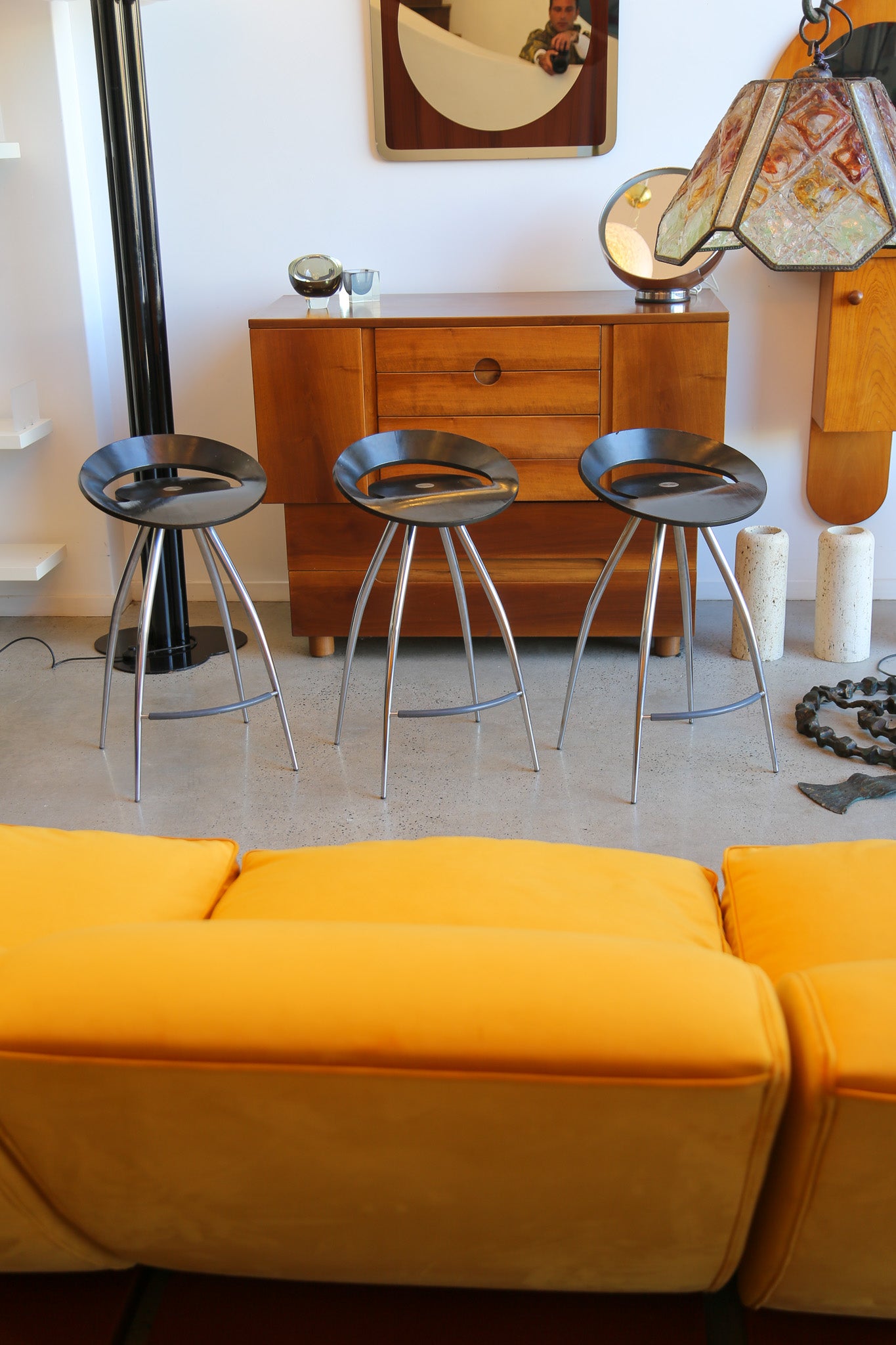 Yellow sofa with three metal stools in a room with wooden furniture and decorative items.
