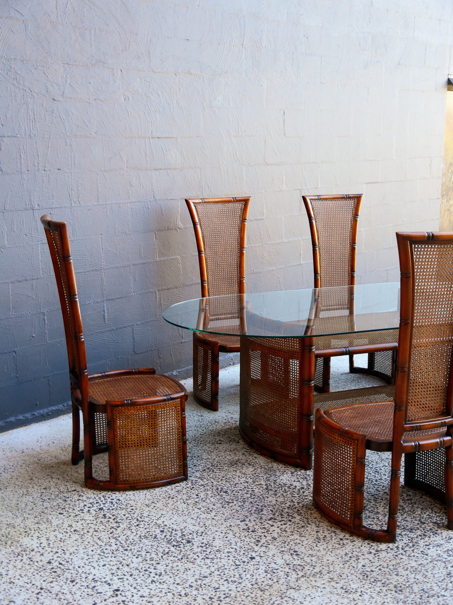 Italian dining set with glass table and four wooden chairs by Marzio Cecchi against a gray brick wall.